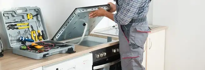 Cooktop repair technician lifting a built-in stovetop for service in Springfield, MO