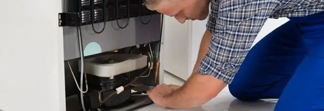 Refrigerator repair technician servicing the compressor and condenser area in Springfield, MO