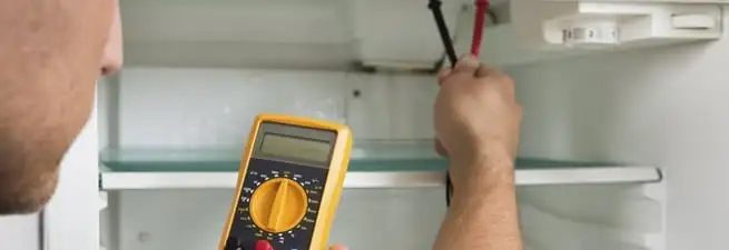 Refrigerator repair technician testing electrical components with a multimeter in Springfield, MO