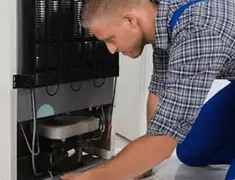 Refrigerator repair technician servicing the compressor and condenser area in Springfield, MO